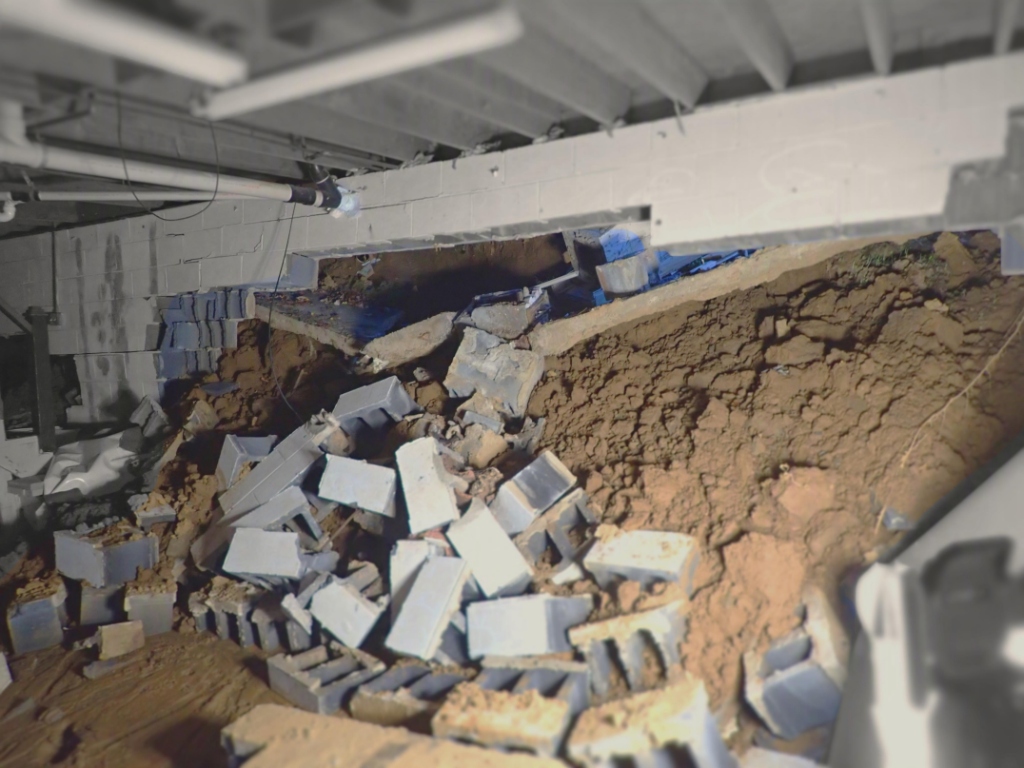 Structural damage showing collapsed block wall with soil intrusion